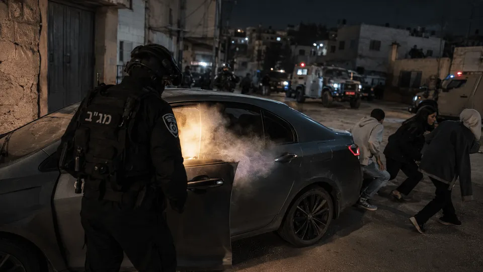 לוחם מג"ב עומד ליד רכב אזרחי ברחוב עירוני חשוך בקלנדיה, בזמן שעשן ואור חזק נראים מתוך הרכב ונוסעים נמלטים לצד השני, על רקע כוחות ביטחון וכלי רכב מבצעיים.